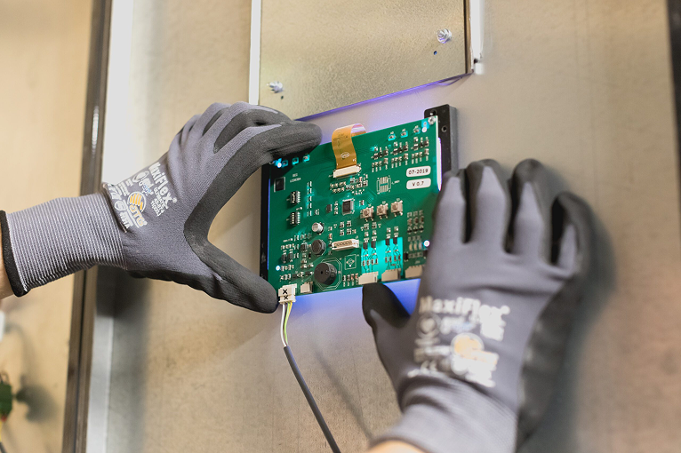 Een persoon plaatst een groene printplaat tegen een metalen wand.