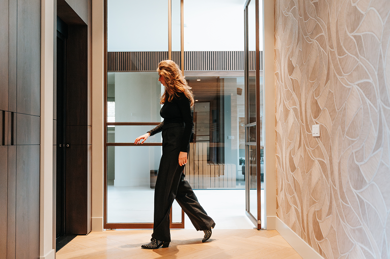 Vrouw in zwart outfit wandelt door een moderne hal met glazen deuren.