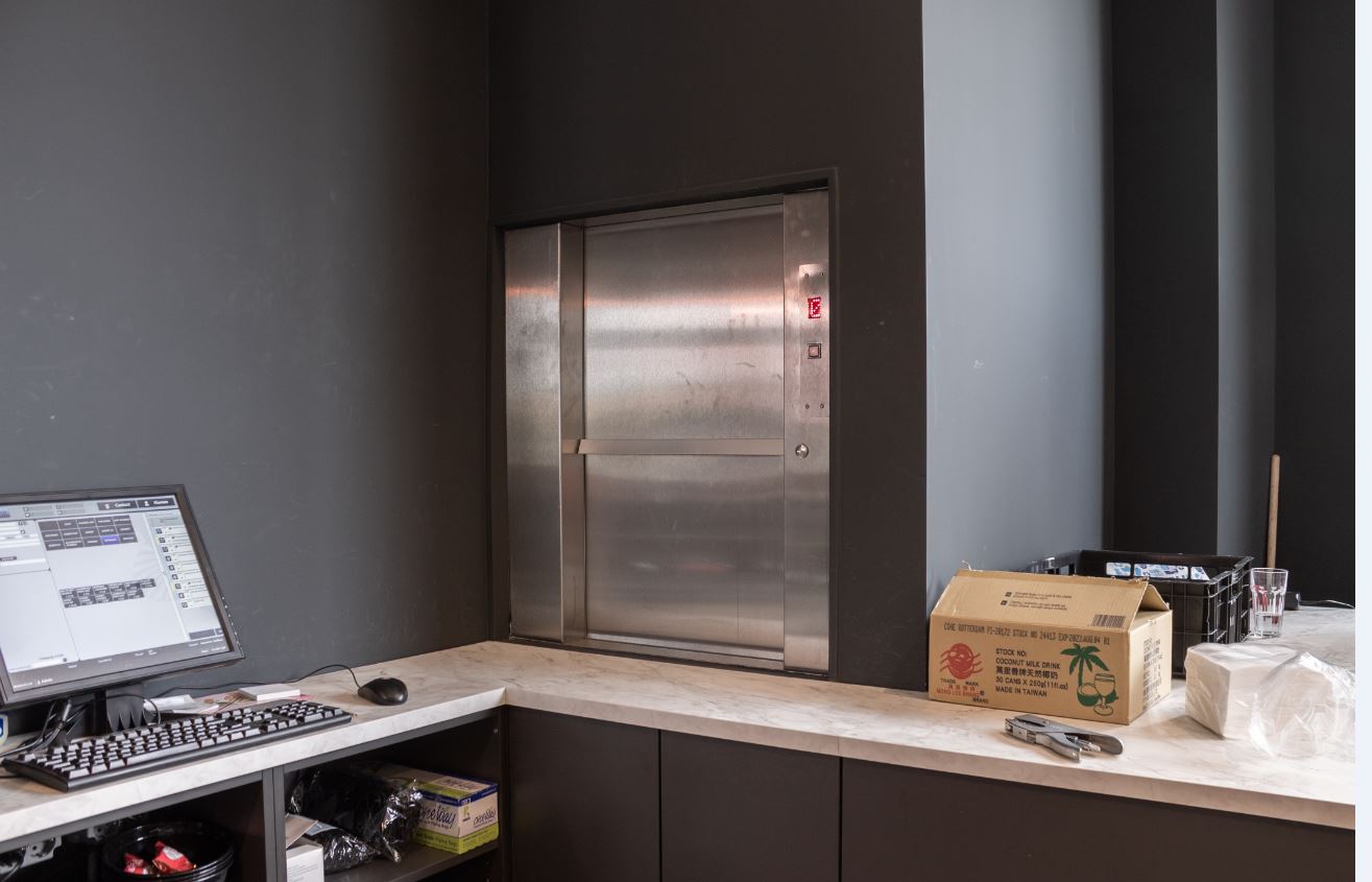 Kantoorruimte met computer, liftdeur en dozen op een marmeren tafel.